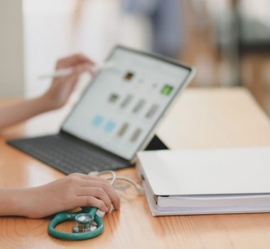 Cropped shot of young female doctor examining medical report while using tablet